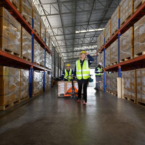 Worker in auto parts warehouse use a handcart to work to bring the box of auto parts into the storage shelf of the warehouse waiting for delivery to the car assembly line